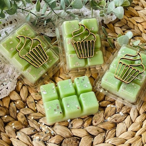 Könnte beinhalten: Drei Wachs-Schmelzen in durchsichtigen Plastikbehältern mit grünem Wachs und Glitzer. Jeder Behälter hat einen goldenen Cupcake-Ausschnitt oben drauf.