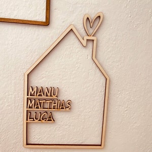 May include: Wooden house-shaped sign with the names Manu, Matthias, and Luca written on it. The house has a heart-shaped chimney.