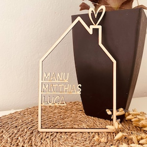 May include: Wooden house-shaped sign with the names Manu, Matthias, and Luca written on it. The sign has a heart-shaped chimney on top.