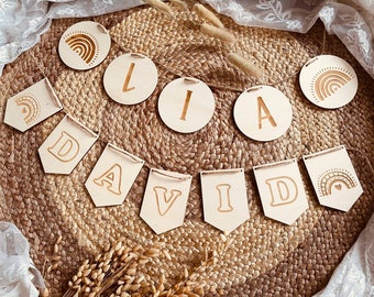 Peut inclure: Une bannière en bois avec le nom "DAVID" écrit en lettres individuelles en bois. Chaque lettre est décorée d'un petit arc-en-ciel et d'un cœur. La bannière est reliée par une ficelle et est suspendue à un fond tissé naturel.