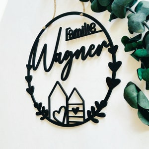 May include: Black wooden wreath with the text "Familie Wagner" and two stylized houses with hearts.