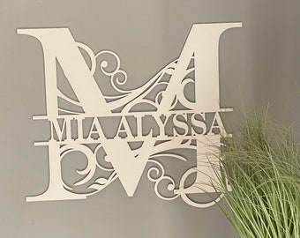 Puede incluir: Letra M de madera blanca con decoración de volutas y los nombres "Mia Alyssa" recortados en el centro.