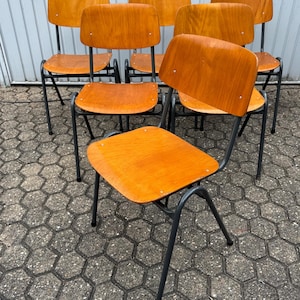 Könnte beinhalten: Sieben Vintage-Holzstühle mit warmem, orangebraunem Finish. Die Stühle haben gebogene Rückenlehnen und Sitze und werden von dunkelgrauen Metallrahmen getragen. Anordnung auf einer strukturierten, grauen Oberfläche.