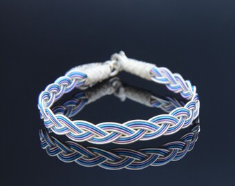May include: A braided silver bracelet with blue and purple accents. The bracelet is made of wire and has a simple, elegant design.
