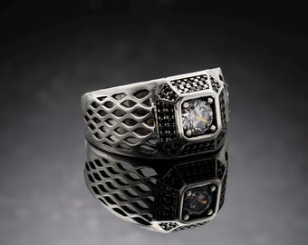 May include: A silver ring with a large, clear cubic zirconia stone set in a square bezel. The ring band is a delicate, openwork design with black accents.