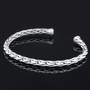 May include: A silver braided bangle bracelet with a smooth, polished finish.