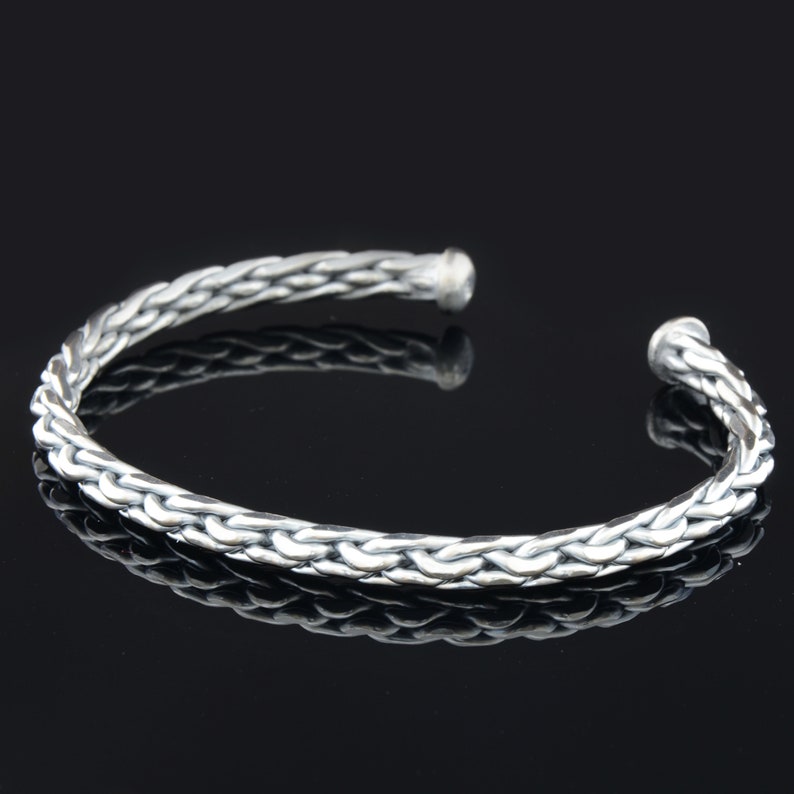 May include: A silver braided bangle bracelet with a smooth, polished finish.