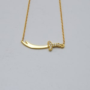 May include: A gold chain necklace with a sword pendant. The sword is decorated with small, clear stones.