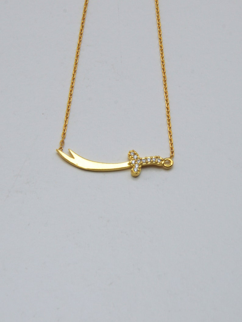 May include: A gold chain necklace with a sword pendant. The sword is decorated with small, clear stones.