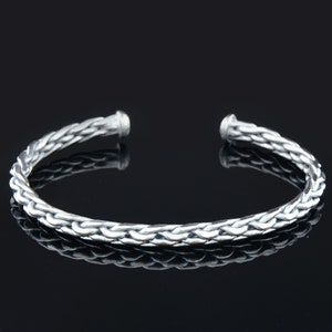May include: A silver braided bangle bracelet with a smooth, polished finish.