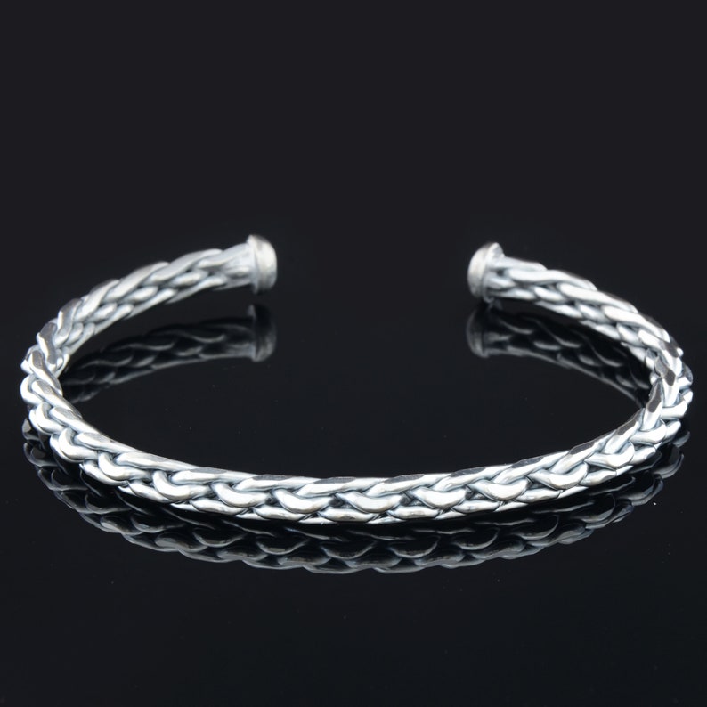 May include: A silver braided bangle bracelet with a smooth, polished finish.