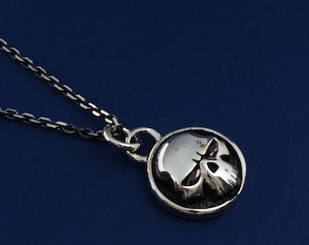 May include: A silver chain necklace with a round pendant featuring a skull with red eyes.
