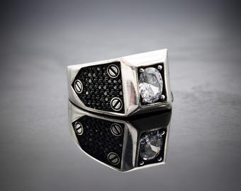 May include: A silver ring with a black stone and a clear stone set in a geometric design.