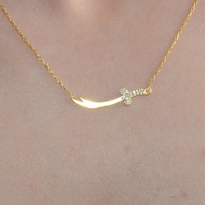 May include: A gold necklace with a small, diamond-encrusted sword pendant.
