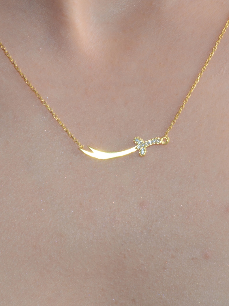 May include: A gold necklace with a small, diamond-encrusted sword pendant.