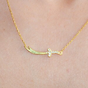 May include: A gold necklace with a small, diamond-encrusted sword pendant.