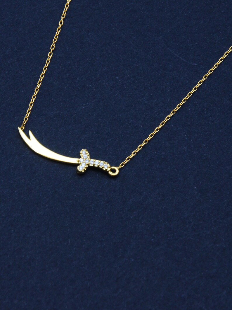 May include: A gold chain necklace with a small, diamond-encrusted sword pendant.