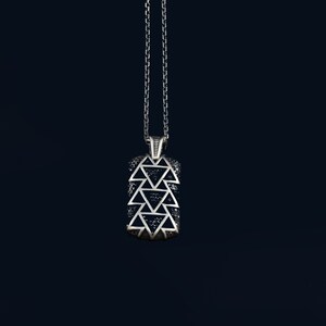 Puede incluir: Un collar de cadena de plata con un colgante que presenta un diseño geométrico de triángulos negros.