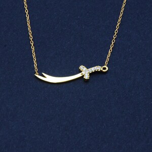 May include: A gold chain necklace with a small, diamond-encrusted sword pendant.