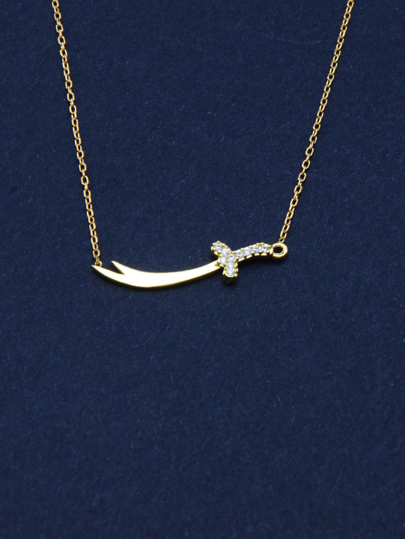 May include: A gold chain necklace with a small, diamond-encrusted sword pendant.