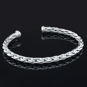 May include: A silver braided cuff bracelet. The bracelet is made of a thick, braided wire and has a simple, elegant design.