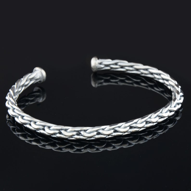 May include: A silver braided cuff bracelet. The bracelet is made of a thick, braided wire and has a simple, elegant design.