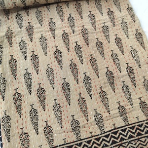 May include: A beige cotton fabric with a repeating pattern of black leaf shapes and red stitching. The fabric has a black and white zigzag border.