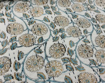 Könnte beinhalten: Weißer Baumwollstoff mit einem blauen und braunen Blumendruck. Der Stoff zeigt ein sich wiederholendes Muster aus stilisierten Blumen mit einem zentralen Kreis und Blütenblättern.