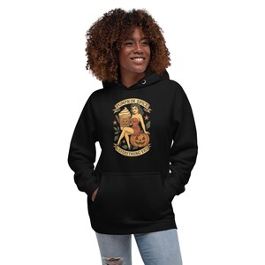 May include: Black hoodie featuring a graphic of a woman, a pumpkin, and a coffee drink. The graphic includes the text "Pumpkin Spice & Everything Vice" in a banner. The hoodie has a drawstring hood and a front pocket.