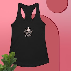Op de afbeelding: Zwart racerback tanktop met de tekst "Crystal Babe" in lichtroze script. De afbeelding bevat een halve maan en een kristalontwerp. De tanktop is gemaakt van een zacht materiaal.