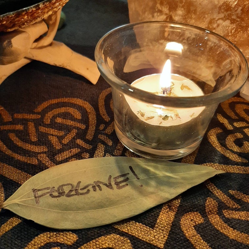May include: A lit candle in a glass jar sits on a dark brown surface with a leaf that says "Forgive!" written on it.