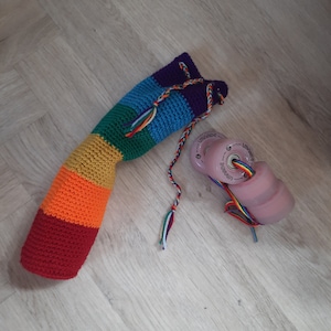 May include: A rainbow crocheted bag with a drawstring closure. The bag is lying on a wooden floor next to a pink skateboard wheel with rainbow laces.