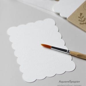 Postkarte aus Aquarellpapier mit stark gewelltem Rand liegt neben einem Stapel an fertig verpackten Postkarten-Sets