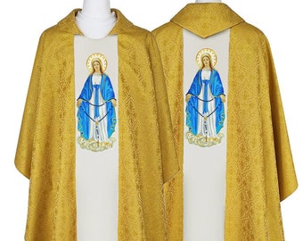May include: Gold-colored liturgical vestment with a floral pattern. The front features a white panel with an embroidered image of the Virgin Mary in blue and white. The vestment has a white lace trim at the bottom and is displayed on a mannequin.