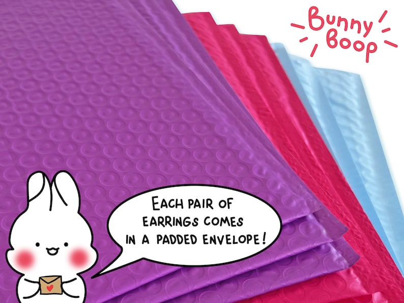 Puede incluir: Sobres acolchados de color morado, rosa y azul con el texto "&iexcl;Cada par de pendientes viene en un sobre acolchado!" y un conejito de dibujos animados que sostiene un sobre peque&ntilde;o con un coraz&oacute;n. El texto "Bunny Boop" est&aacute; escrito con una fuente divertida encima de los sobres.