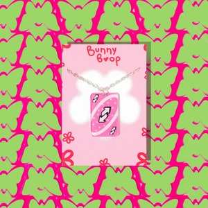 May include: A pink Uno card necklace with a silver chain. The card features a white reverse arrow symbol and the text "Bunny Boop" is on the card.