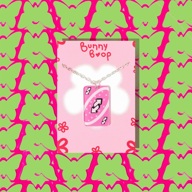May include: A pink Uno card necklace with a silver chain. The card features a white reverse arrow symbol and the text "Bunny Boop" is on the card.