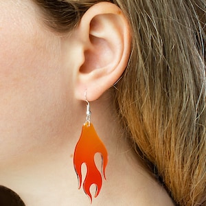 Può includere: Un paio di orecchini a forma di fiamma di colore arancione e rosso con ganci argentati.