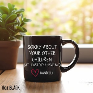 May include: Black ceramic coffee mug with white text that reads "Sorry about your other children. (At least you have me)" and a red heart with the name "Danielle" below it.