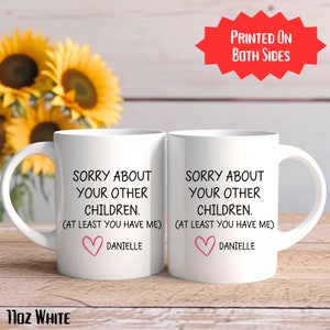 May include: Two white ceramic mugs with black text that reads "Sorry about your other children. (At least you have me) Danielle" and a pink heart. The mugs are printed on both sides.