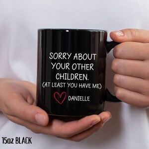 May include: A black 15oz mug with white text that reads "Sorry about your other children. (At least you have me)" and a red heart with the name "Danielle" below it.
