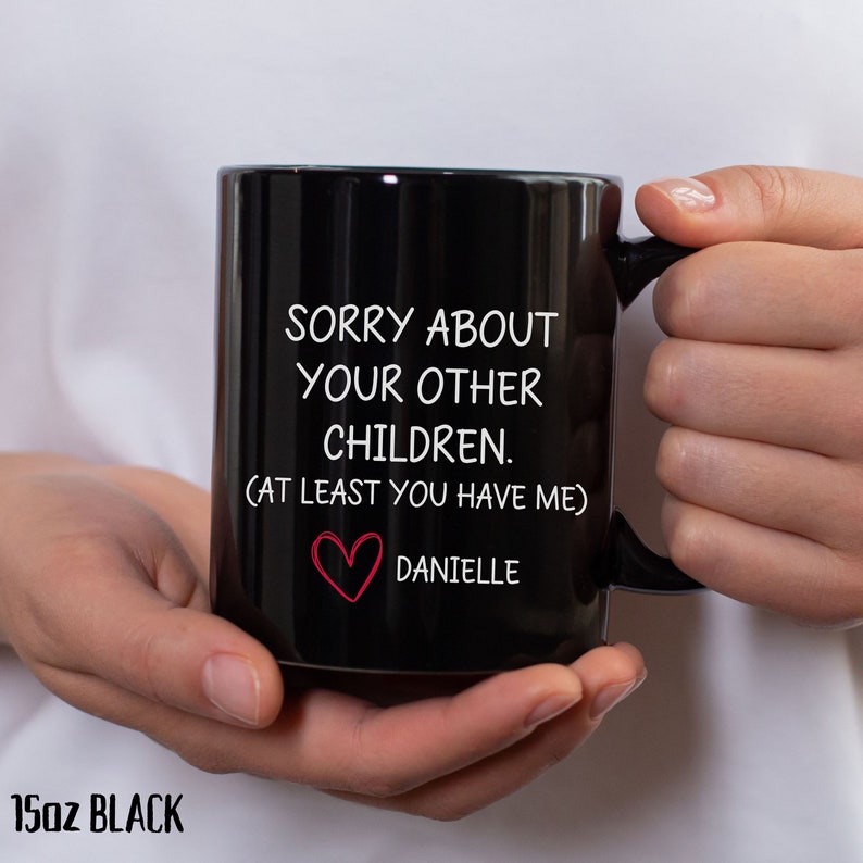 May include: A black 15oz mug with white text that reads "Sorry about your other children. (At least you have me)" and a red heart with the name "Danielle" below it.