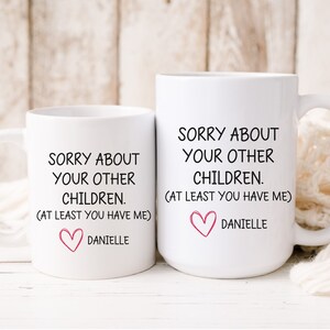 May include: Two white coffee mugs with black text that reads "Sorry about your other children. (At least you have me)" and a pink heart with the name "Danielle" below.