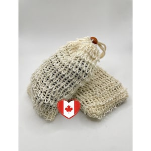 May include: Two beige, open-weave soap saver bags with a drawstring closure and wooden bead. The bags are filled with dark-colored soap. A red and white heart-shaped graphic with a maple leaf is in the foreground.
