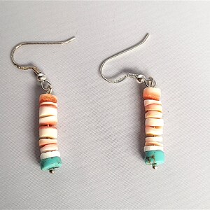 May include: A pair of dangle earrings with a silver hook and a turquoise and white shell bead design.