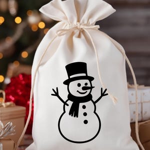 May include: A cream-colored drawstring gift bag featuring a black snowman design. The snowman has a top hat, scarf, and stick arms. The bag is tied at the top with a matching drawstring, perfect for holiday gifting.
