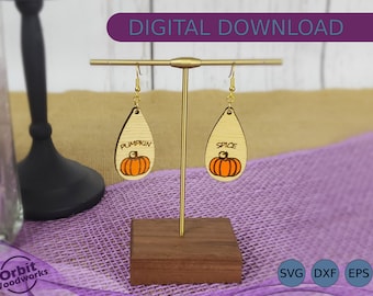 May include: A pair of wooden pumpkin-shaped earrings with gold hooks. The earrings are teardrop-shaped and have the words "Pumpkin" and "Spice" written on them.