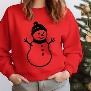 May include: A red sweatshirt featuring a black snowman graphic. The snowman has a black hat, scarf, and three buttons. The sweatshirt is a solid red color, perfect for the holiday season.