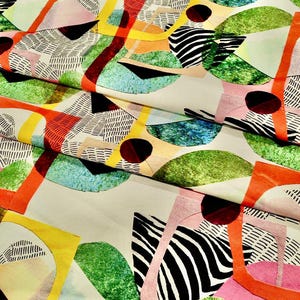 Könnte beinhalten: Abstraktes Gewebe mit einem farbenfrohen geometrischen Design. Das Muster zeigt Formen in Grün, Gelb, Orange, Rosa und Schwarz mit Bereichen mit gestreiften und gepunkteten Texturen. Der Stoff hat einen hellbeigen Hintergrund.