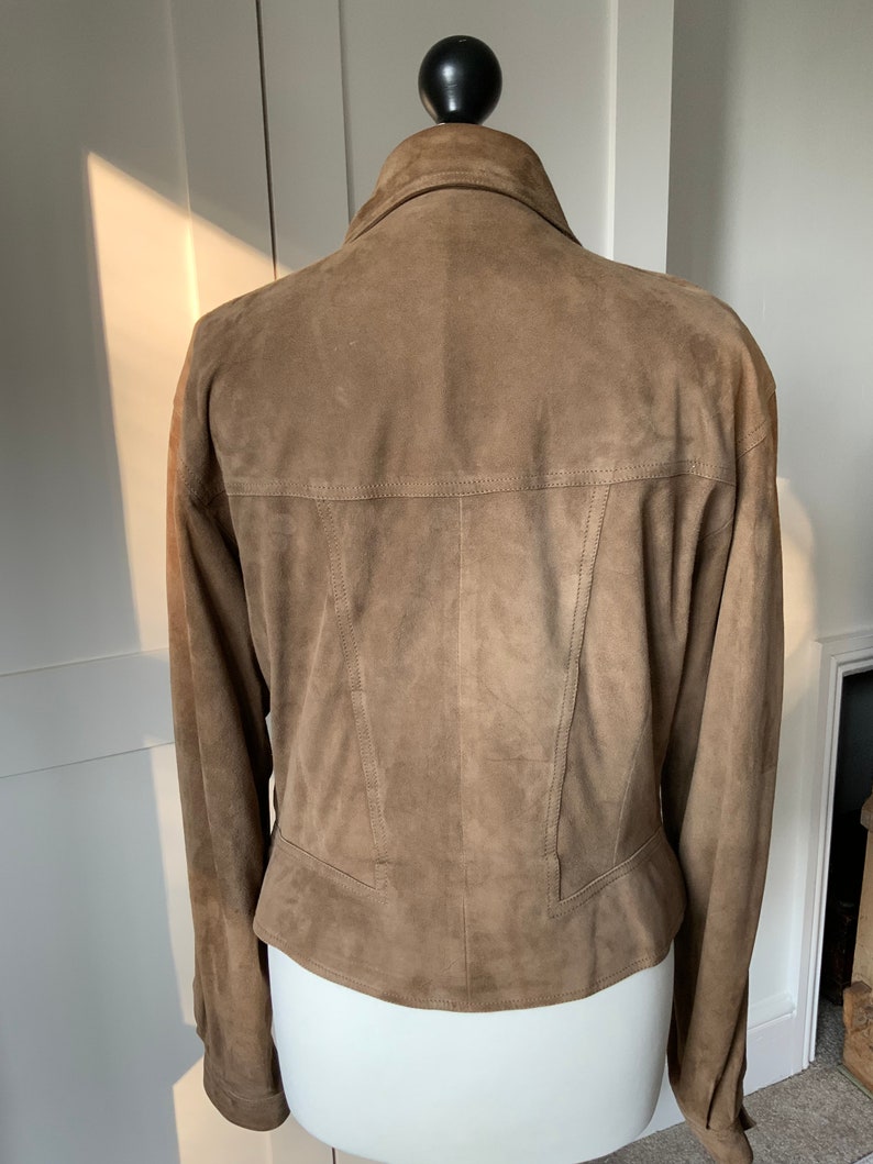 K&ouml;nnte beinhalten: Eine braune Wildlederjacke mit Kragen und langen &Auml;rmeln. Die Jacke hat eine figurbetonte Silhouette und eine verk&uuml;rzte L&auml;nge.